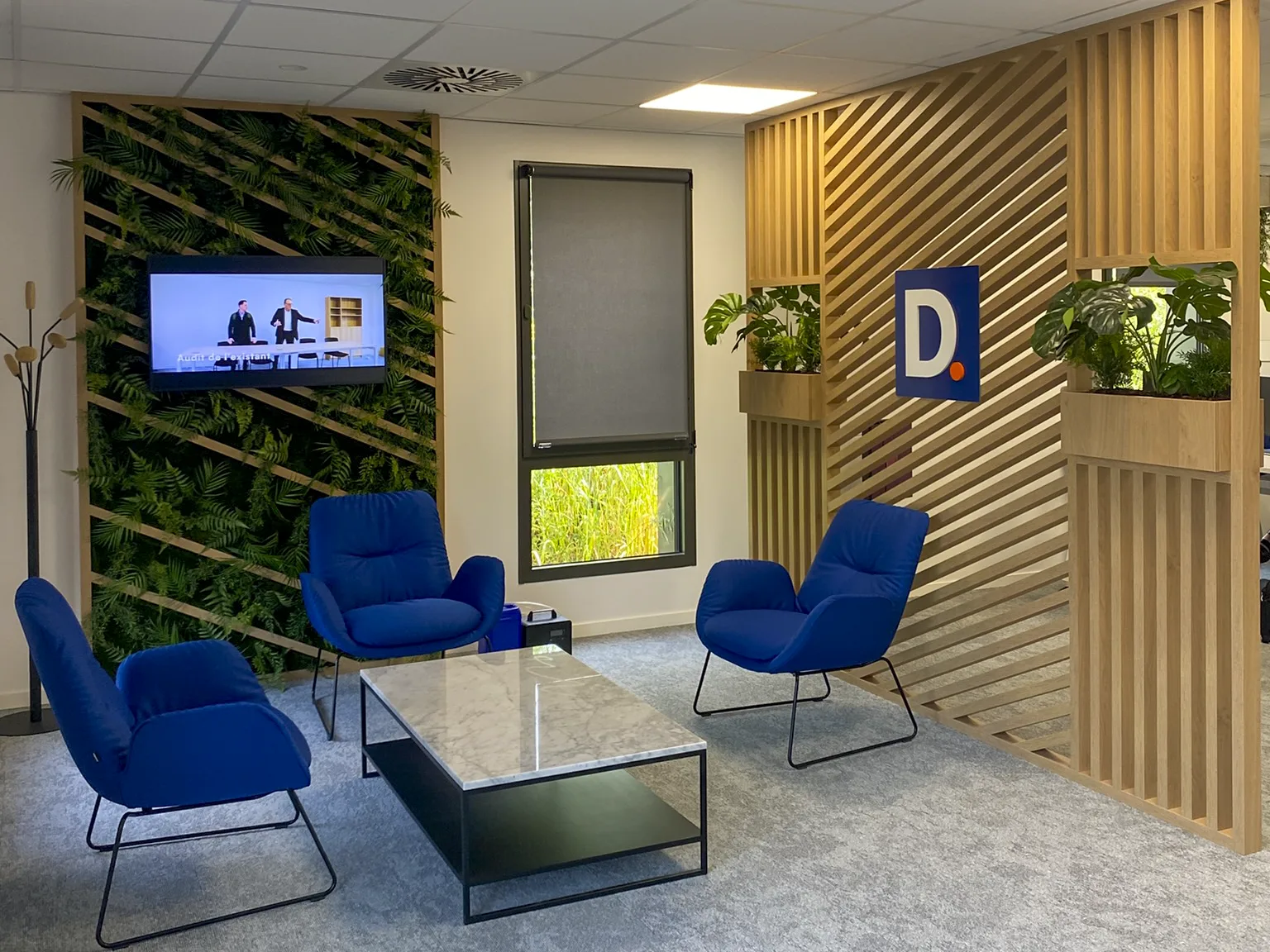 Espace d'accueil de bureaux avec mur végétal, claustra en bois et fauteuils bleus, aménagé par LIV Intérieur