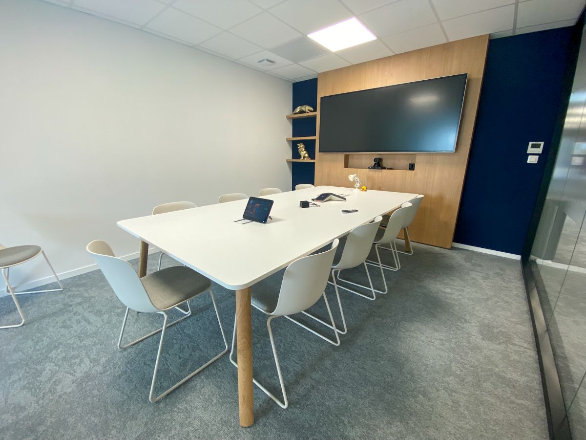 Salle de réunion à Rennes avec grande table blanche, chaises blanches, écran mural sur panneau bois et mur bleu nuit, aménagée par LIV Intérieur
